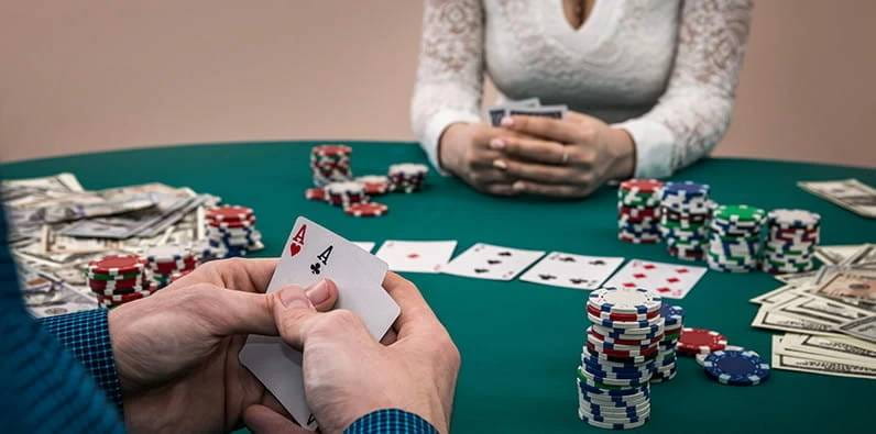 Una mesa de casino con cartas, fichas y dinero en efectivo en pilas y un jugador con dos ases en las manos.