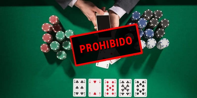 Una mesa de casino con fichas, cartas de póker y unas manos teniendo un móvil.