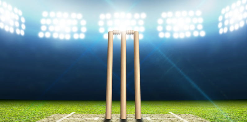 Una pelota roja, unos guantes y un bate de críquet en el césped de un estadio