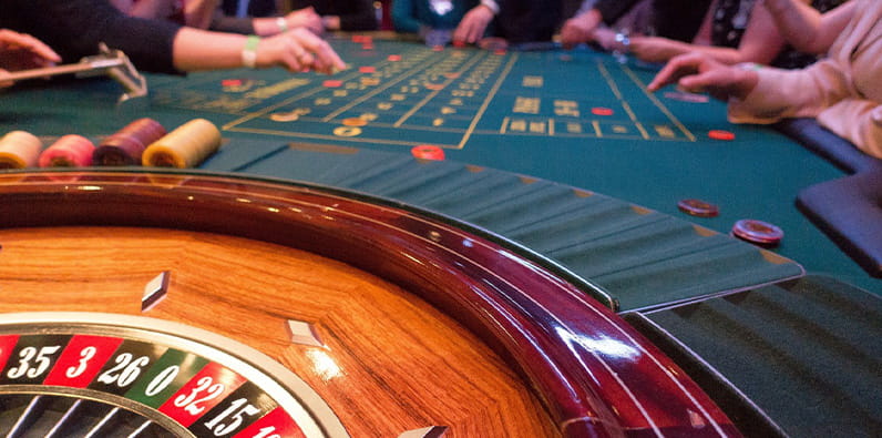 Mesa de ruleta de casino con varias personas alrededor.