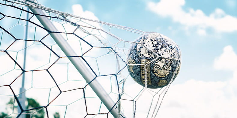Un balón de fútbol marca gol dentro de una red, con un cielo azul despejado de fondo.