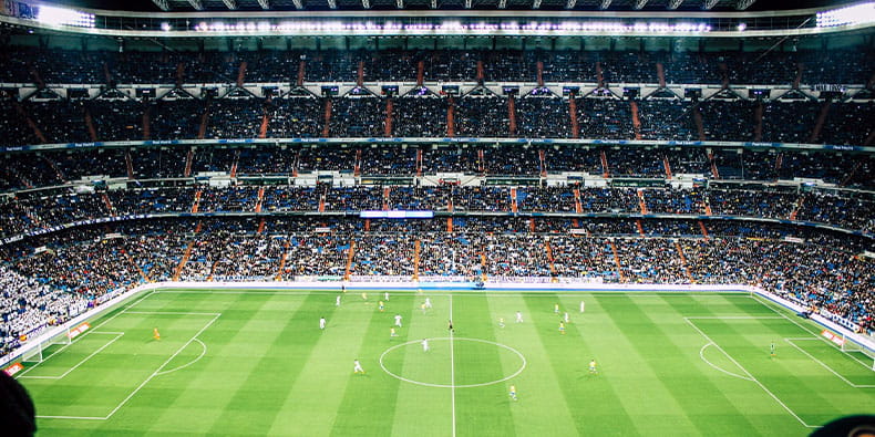 Un amplio estadio de fútbol iluminado durante un partido en juego, con muchos jugadores en el campo.