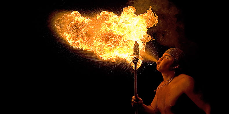 Foto de la fiesta Correfoc. Un hombre disfrazado hace una gran llama de fuego con su boca.