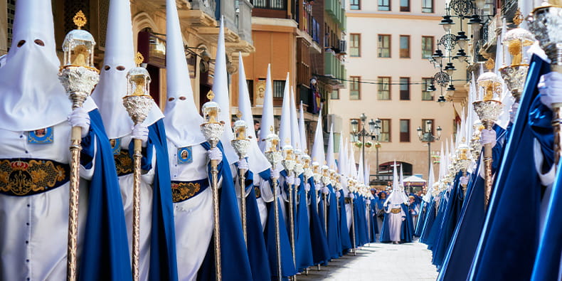 Foto de la Semana Santa. Dos líneas de nazarenos vestidos en azul y blanco sujetan el cetro de su cofradía.