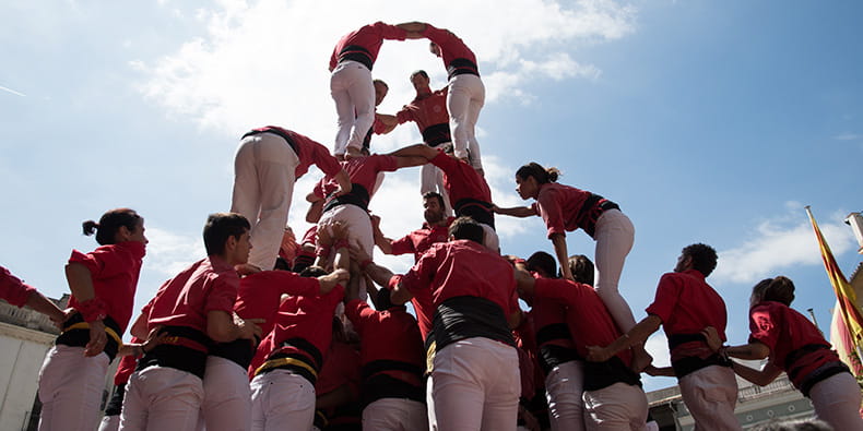 Foto de los Castells i Muixeranga. Una gran torre humana de varios metros de altura con camisetas de color lila.