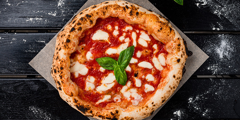 Una pizza margarita con albahaca de estilo italiano, servida en un plato blanco, de fondo un mosaico de círculos negros. 
