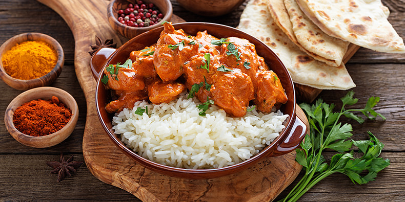 Plato de tikka masala con arroz decorado con perejil sobre una mesa blanca, con una servilleta al lado. 