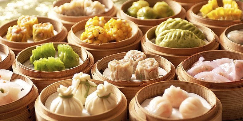 Selección de platos dim sum, incluyendo dumplings y wantons, dispuestos en una mesa con platos y pequeñas cestas-vaporeras.