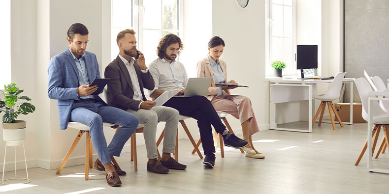 Cuatro jóvenes sentados en sillas esperando a una entrevista de trabajo en España.