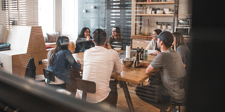 Un equipo de personas con reducción de la jornada laboral en un comedor del trabajo conversando alrededor de una mesa.